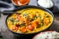 A vibrant curry with chunks of sweet potato, whole cherry tomatoes and fresh green herbs scattered on top.